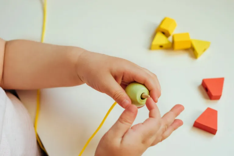 Dettaglio di bambino che gioca a infilare una corda in una biglia di legno per stimolare attenzione