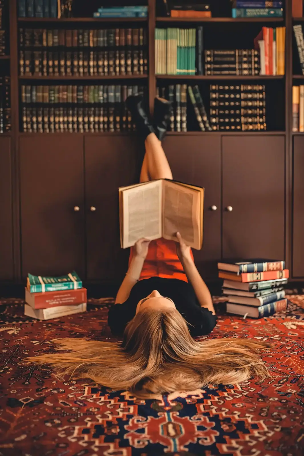 Una ragazza è sdraiata sul pavimento della biblioteca e sta leggendo un libro