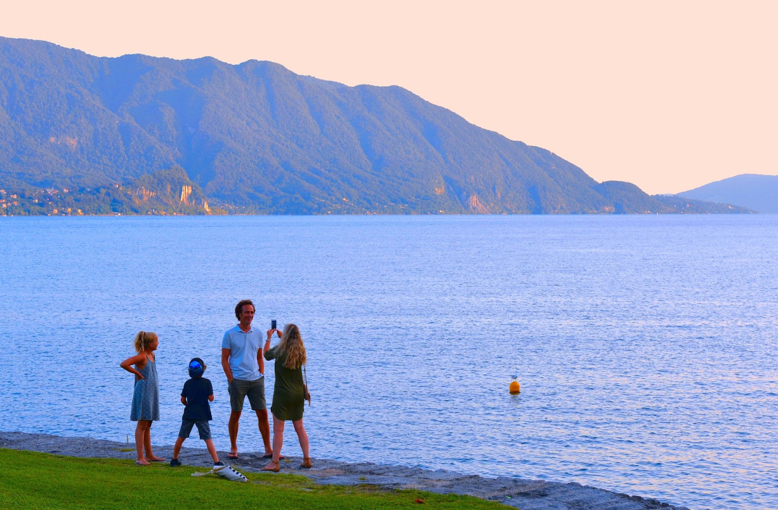 Famiglia felice sulla spiaggia vuota alla fine di una giornata estiva con lago e montagne sullo sfondo a Cannero, Verbania Italia