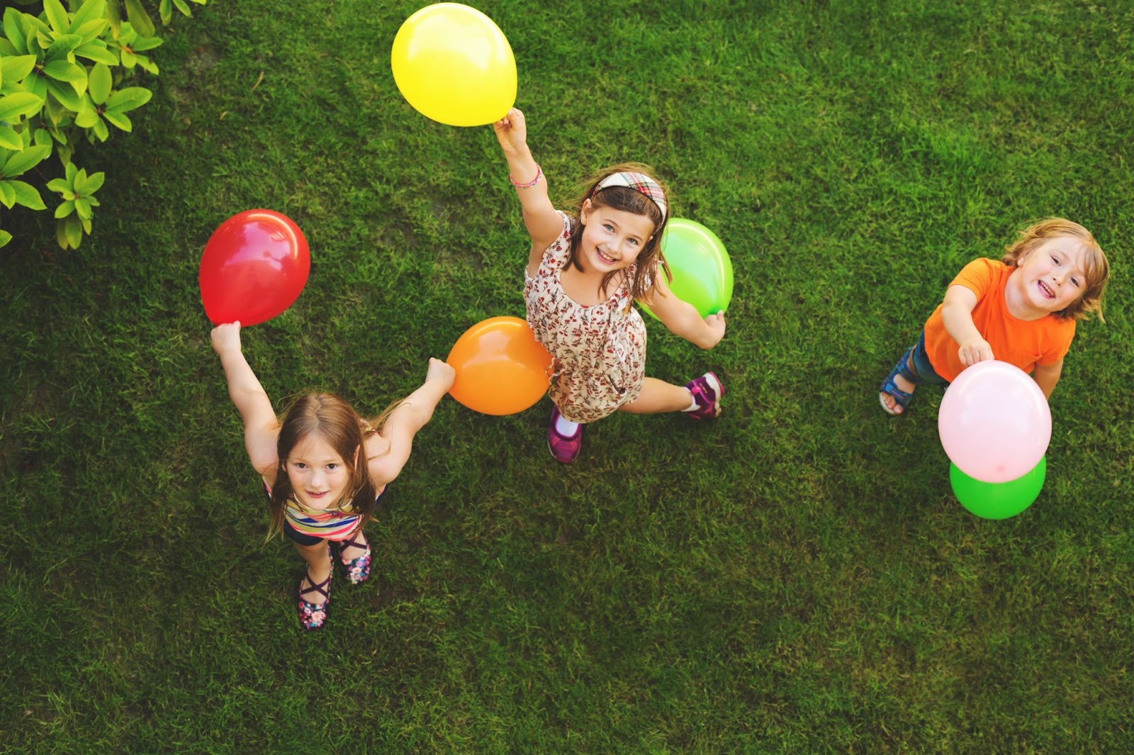 Tre bambini felici giocare con palloncini colorati all'aperto, vista dall'alto