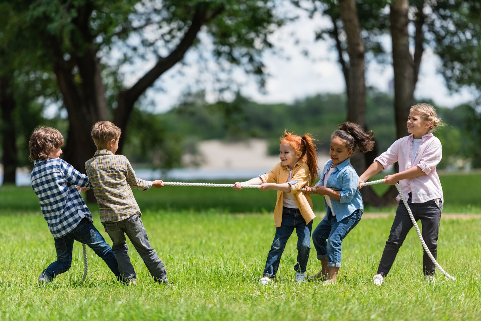 vista laterale di bellissimi bambini multietnici che giocano a tiro alla fune nel parco