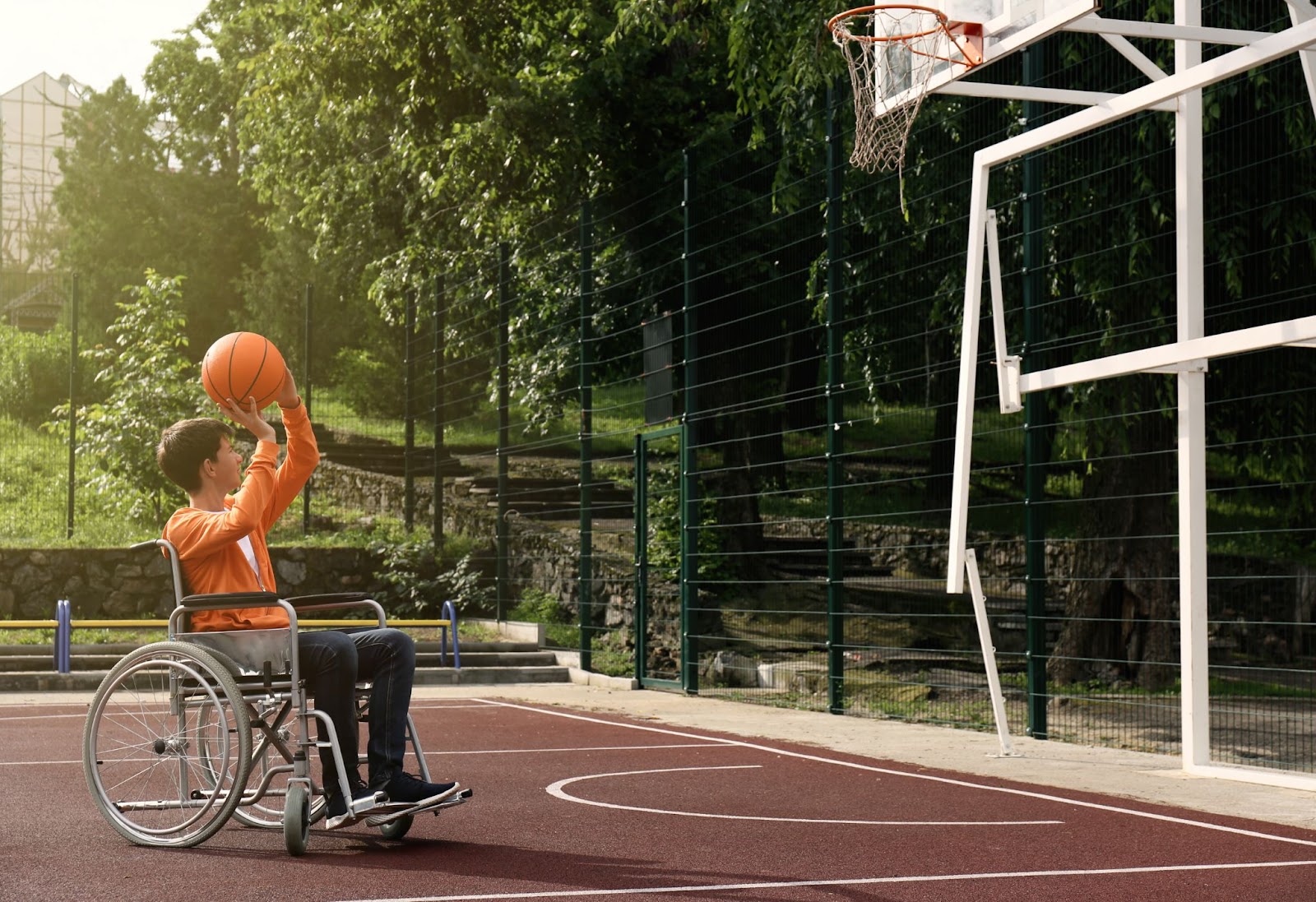 Un adolescente disabile in sedia a rotelle gioca a basket su un campo all'aperto